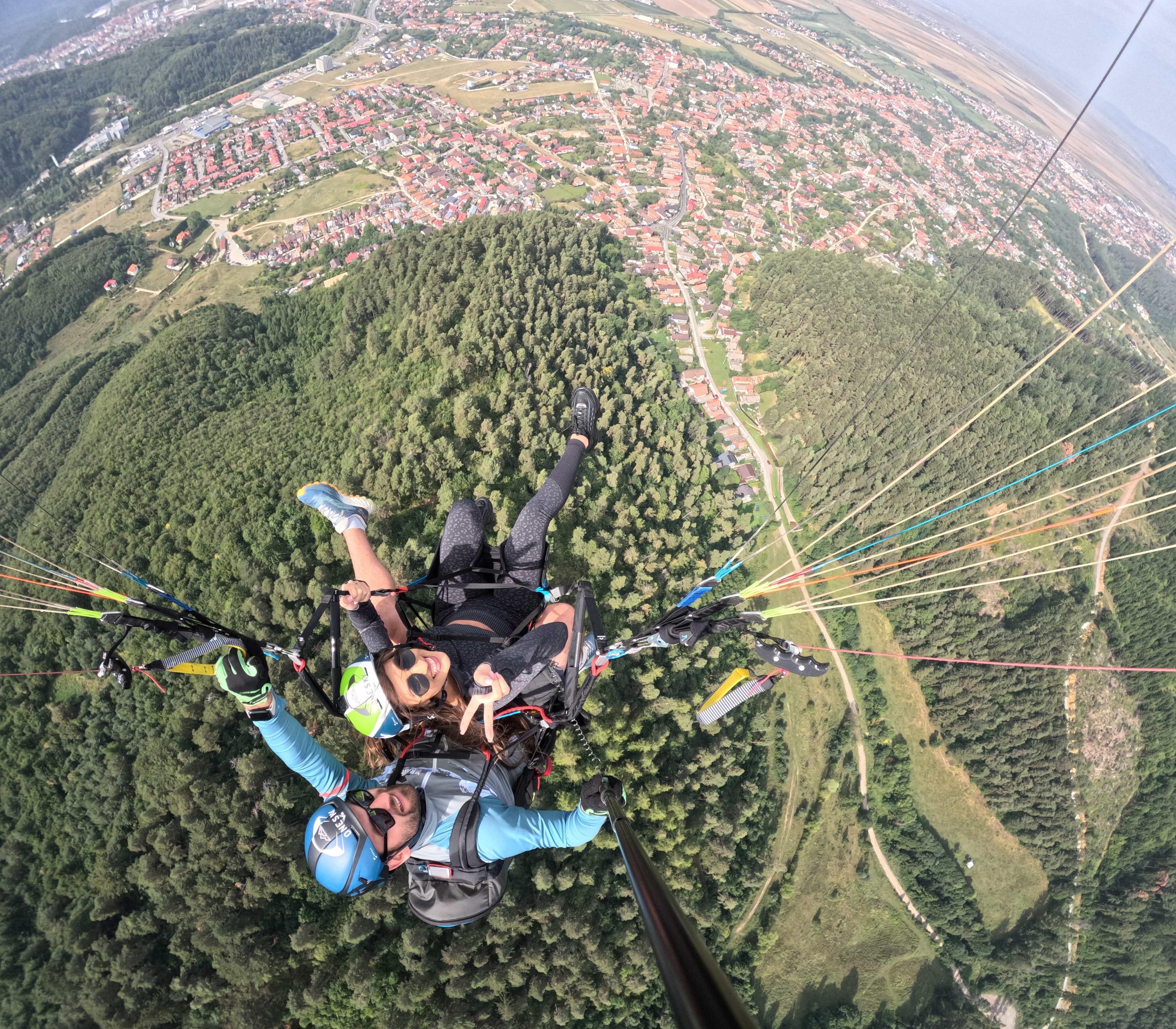 Pasageră zâmbind și făcând semnul păcii în zbor, deasupra pădurii verzi și a cartierelor Brașovului